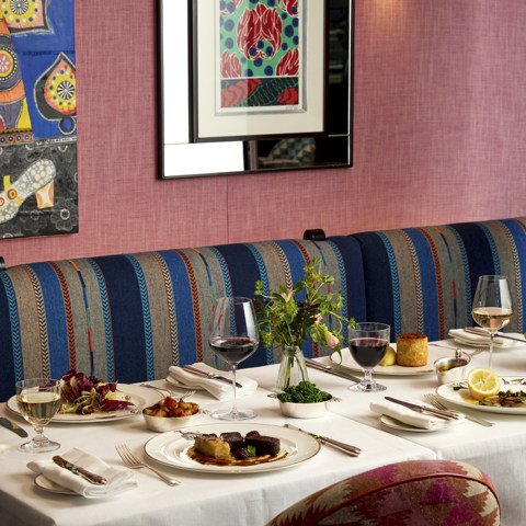 A table of four laid with main dishes accompanied by glasses of wine at Brumus. The table is positioned in front of banquette seating with art hanging on the wall