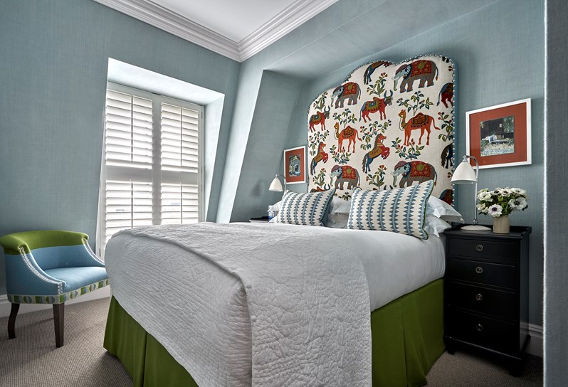 Diagonal bedroom shot a superior room with plain light blue walls, colourful animal drawings on the headboard and blue and green tones in the rest of the room.