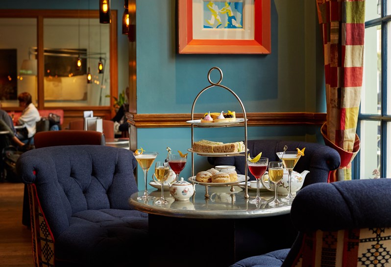 An image of the Afternoon Tea with a Twist at Oscar, Charlotte Street Hotel. The table displays the afternoon tea set up and cocktails.