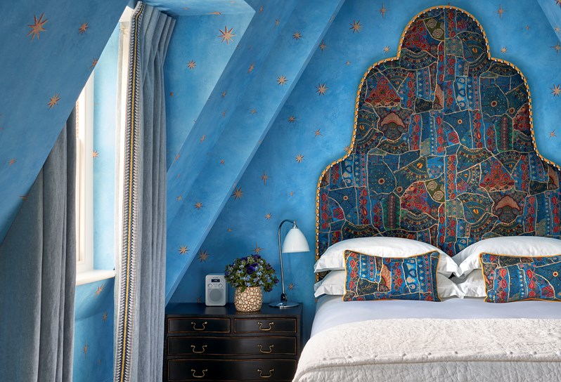 A spacious bedroom with bright blue walls and a queen size bed with colorful fabric headboard