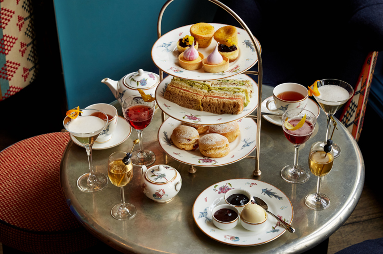 An image of the Afternoon Tea with a Twist at Oscar, Charlotte Street Hotel. The table displays the afternoon tea set up and cocktails. 