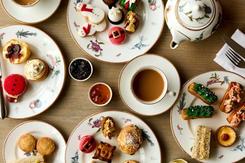 Festive Afternoon Tea shot from above. Cups of tea and plates of cakes and sandwiches laid on a table on Mythical Creatures crockery