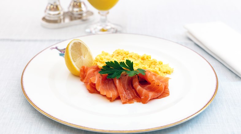 Smoked salmon with scrambled eggs and half a fresh lemon. In the background is a glass of orange juice.