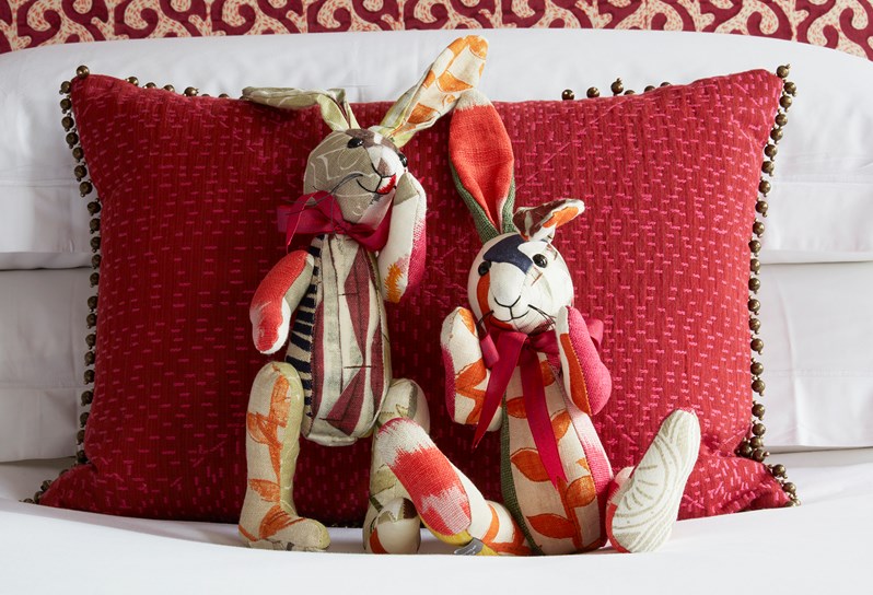 Kit Kemp's patchwork soft toys including two colourful patchwork rabbits in the foreground, a red soft cushion is the background