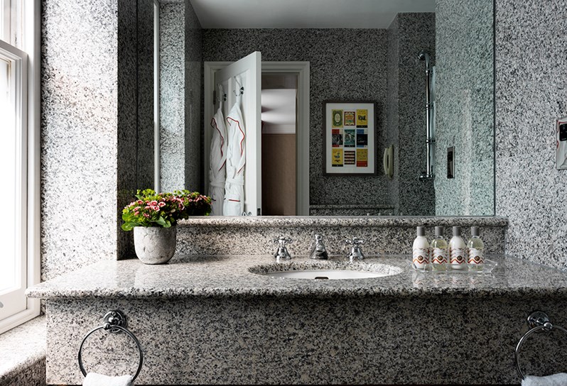 A granite bathroom containing a deep bathtub with a TV in the wall, two pedestal basins with mirrors hung above and a free standing shower.