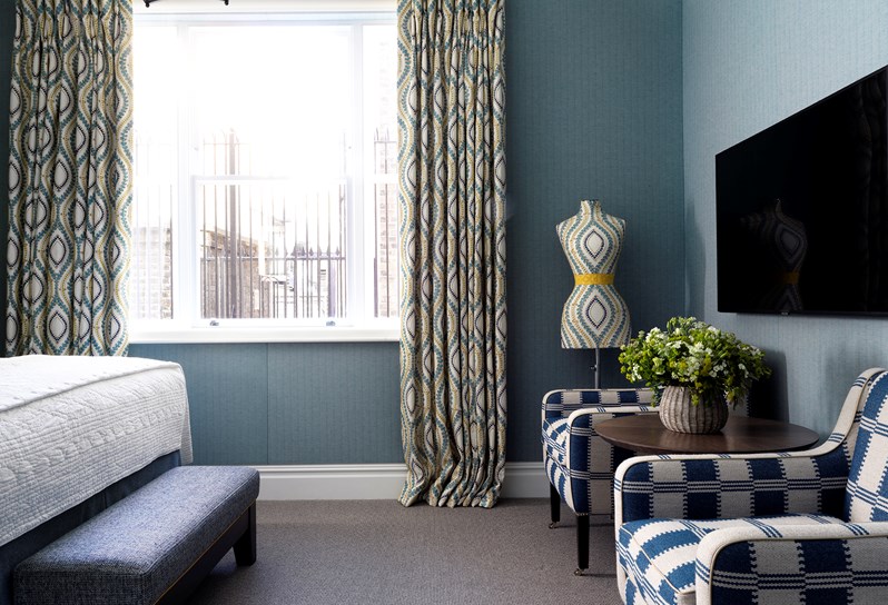 2 blue and white armchairs sit under a television. There are blue and white curtains to the left and the walls are pale blue.
