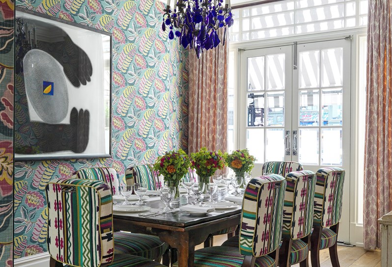The Dora Carrington function room at Charlotte Street Hotel.  A table is set up for dinner service and an ornate blue chandelier hangs above the table. In the background are double French doors.