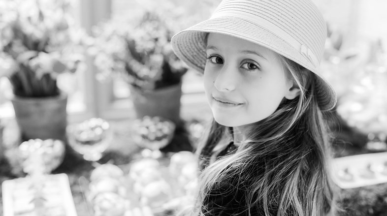 A young girl in a hat with long hair, black and white.