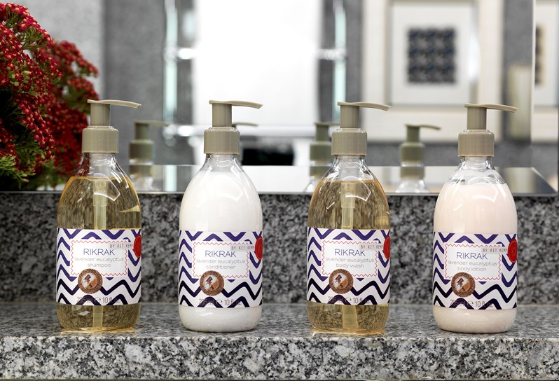 Four large pump bottles of Kit Kemp's own RikRak bathroom range, in the lavender and eucalyptus scent, showcased in front of a mirror in a granite bathroom.