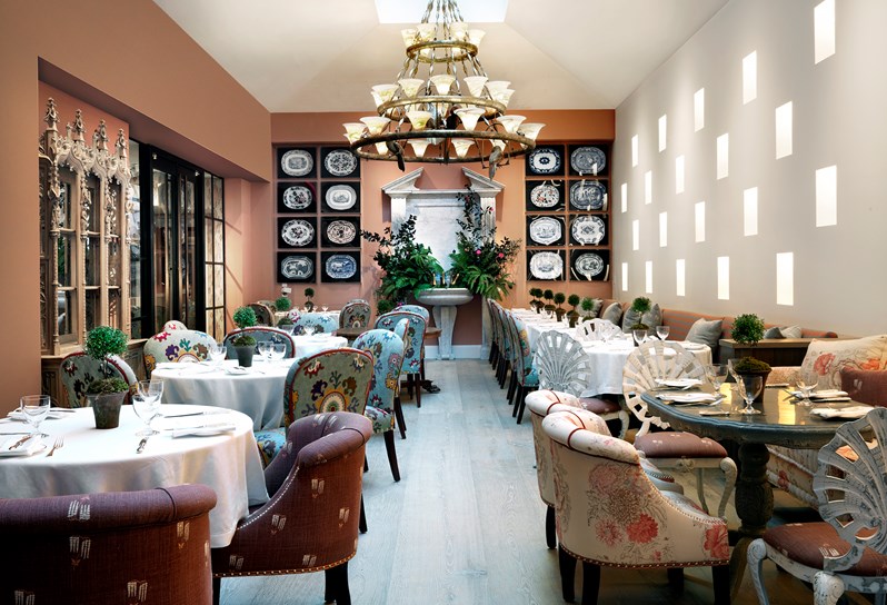 The Orangery with plenty of comfortable seats and tables for dining. A wall with sixteen art pieces showcasing various serving plates scattered around a leafy fountain oasis.