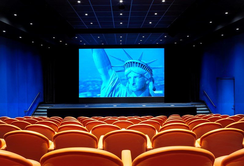 The state-of-the-art screening room with 130 comfortable leather seats in bright coral, projecting the Statue of Liberty on the advanced screen.
