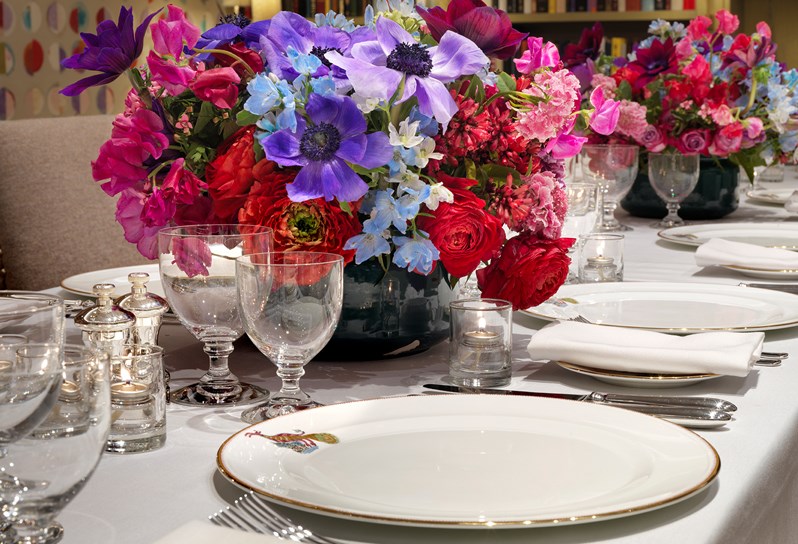 A close up of the beautiful table setting in the Reading Room, containing Kit Kemp's Wedgwood range Mythical Creatures and a stunning flower arrangement in red, pink, purple and blue.