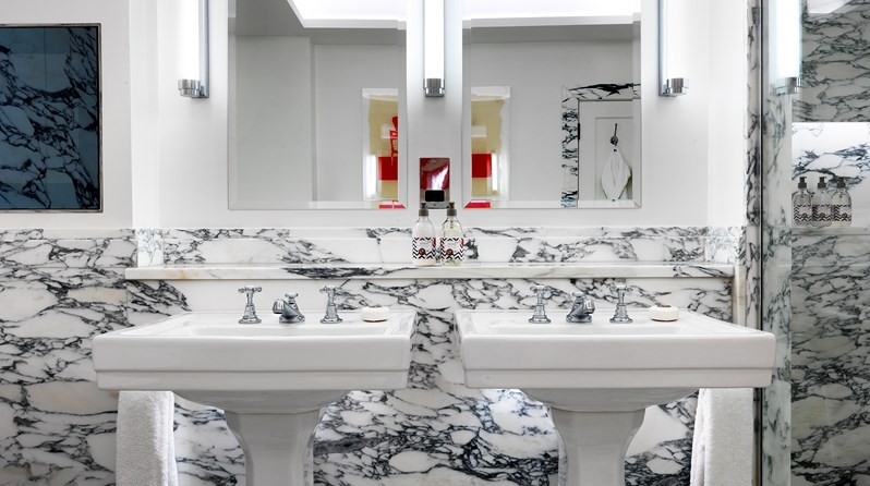 Two separate basins with mirrors hung above each one in a white marble bathroom.