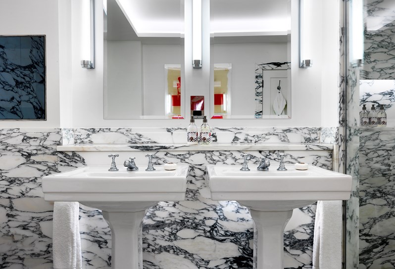 Two separate basins with mirrors hung above each one in a white marble bathroom.