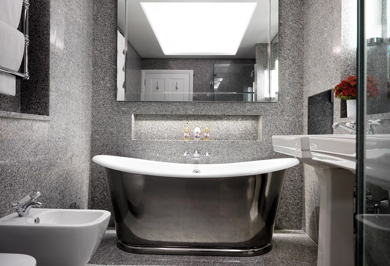 A granite bathroom featuring a free standing chrome bathtub, a walk in shower, two separate basins, a toilet and a bidet, with Kit Kemp's own bathroom range, RikRak, placed throughout.
