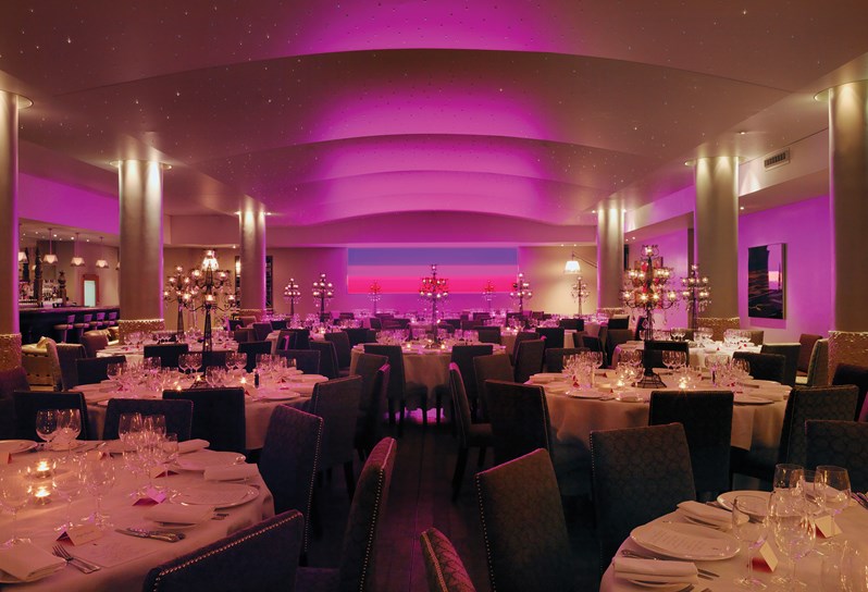 The pool at Haymarket Hotel set for a formal dinner party. Round tables are spread about the room with white table cloths and tall elegant candelabras. A pink light installation is featured on the back wall.