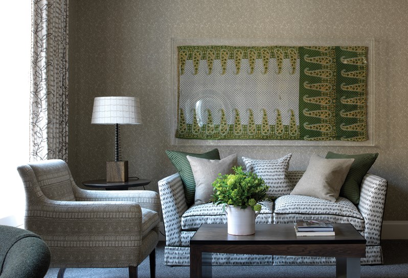 Living room with original artwork, a comfortable sofa with fluffy pillows and an arm chair  in front of a wooden coffee table with fresh flowers and coffee table books.