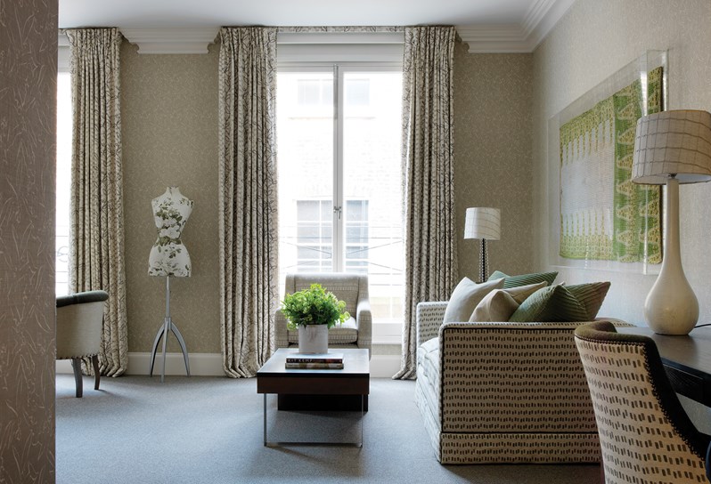 A spacious Junior Suite, showing a patterned wallpaper contrasted by a light green and white sofa, a coffee table, arm chair and a working desk.