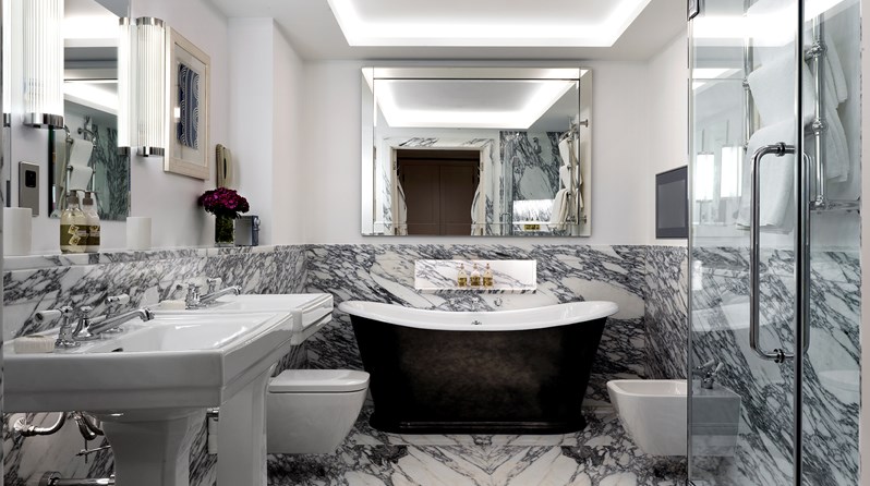 A marble bathroom containing a deep bathtub, a separate walk in shower, double basins, a bidet and a toilet.