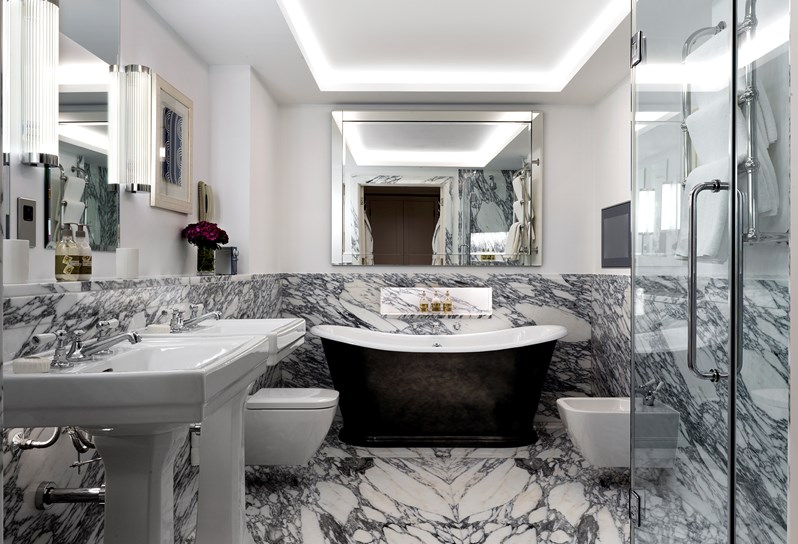 A marble bathroom containing a deep bathtub, a separate walk in shower, double basins, a bidet and a toilet.
