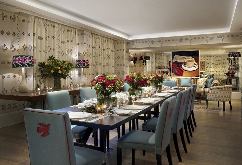 Rocklin room set for a dinner at a long table with candles. The room has dark floral printed wallpaper.