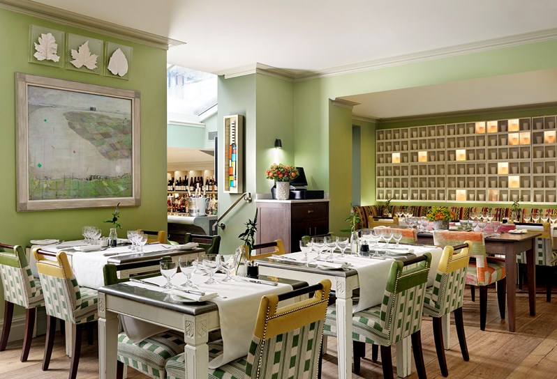 Beautifully set dining tables at The Potting Shed Restaurant in booths and at private tables, looking toward an art installation of illuminated porcelain pots by Martha Freud scattered on a wall.