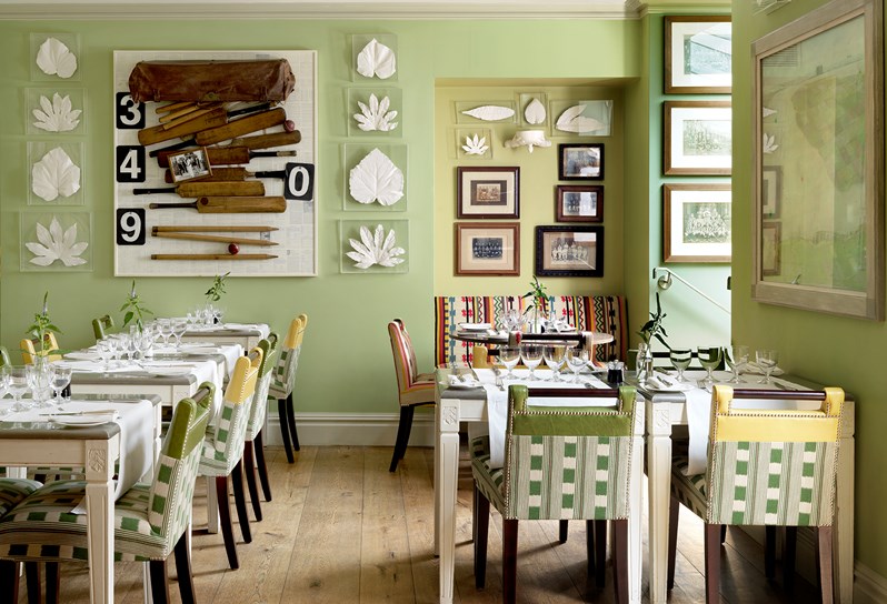Tables beautifully set for dining in the quirky and playfully decorated restaurant, featuring original artwork and a summery green wallpaper.