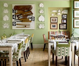 Tables beautifully set for dining in the quirky and playfully decorated restaurant, featuring original artwork and a summery green wallpaper.
