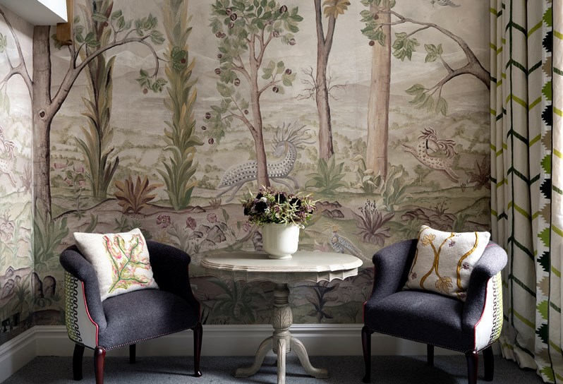 Seating area in one of our mezzanine suites. 2 grey tub chairs, a beige table and a wallpaper with trees