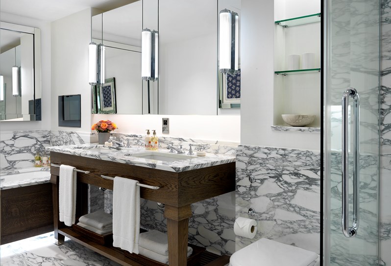 A white bathroom with grey and white marble. There is a double sink with mirrors above along the wall. There is a separate bath and shower.