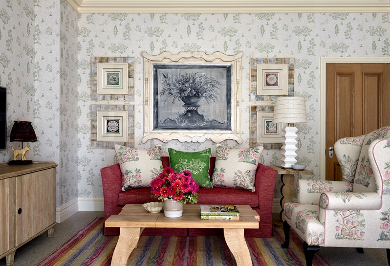 Living room with original artwork, a comfortable sofa with fluffy pillows and an arm chair in the same bold pattern as the pillows in front of a wooden coffee table with fresh flowers and coffee table books.