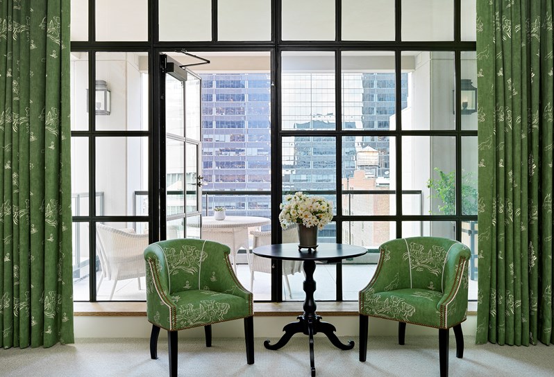 Two green armchair are set in front of floor to ceiling critall windows with views of Manhattan