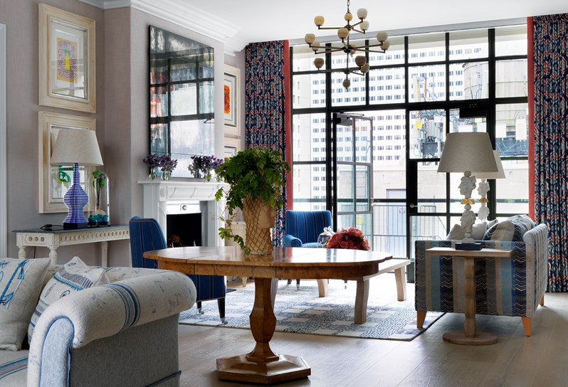 A bright, airy lounge area with a large sofa and two arm chairs with a coffee table, overlooking a spacious terrace, with a statement table containing a flower centerpiece in the forefront.