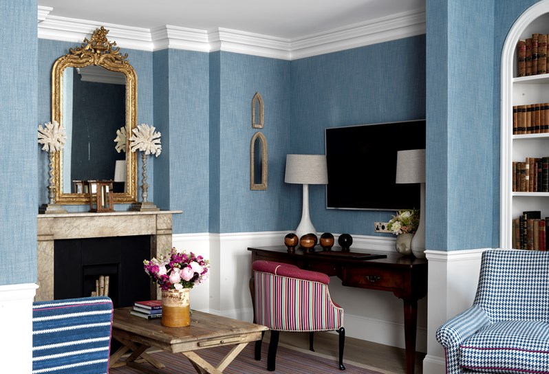 A beautiful gold decorative mirror hangs over the fireplace to the left of the living room. There is a separate nook with a writing desk, a maroon chair and a television.