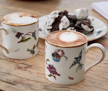 Kit Kemp's Mythical Creatures mugs seen here filled with coffee. The design features a series of characters and patterns that have a primitive, folkloric feel