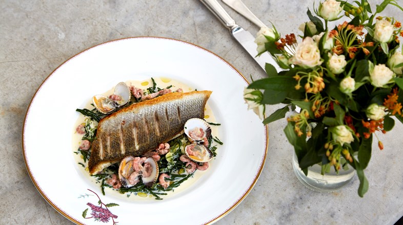 A colourful sea bass dish with clams alongside a small bouquet of flowers