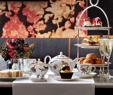Champagne afternoon tea displayed on a table in Refuel restaurant at The Soho Hotel. The fine bone china is Mythical Creatures by Kit Kemp for Wedgwood along side a 3 tier cake stand, sandwiches and scones.