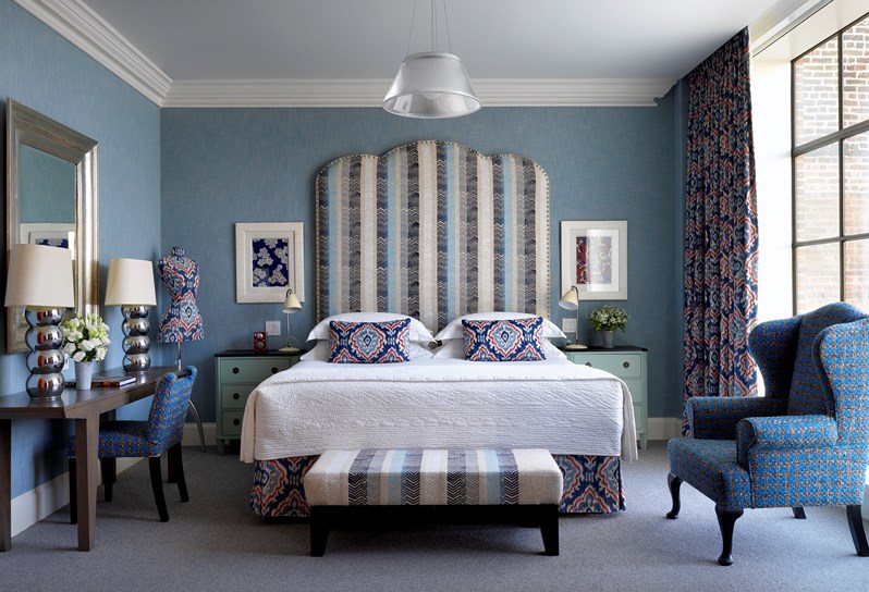 The bedroom room with fresh flowers in a one bedroom suite at the Crosby Street Hotel with vivid blue colour scheme, king size bed, graphic neutral colour scheme and floor length windows with views of the SoHo neighbourhood.