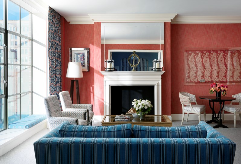 The living room with fresh flowers, several chairs and a sofa in a one bedroom suite at the Crosby Street Hotel with a colourful interior design and floor length windows with views of the SoHo neighbourhood.