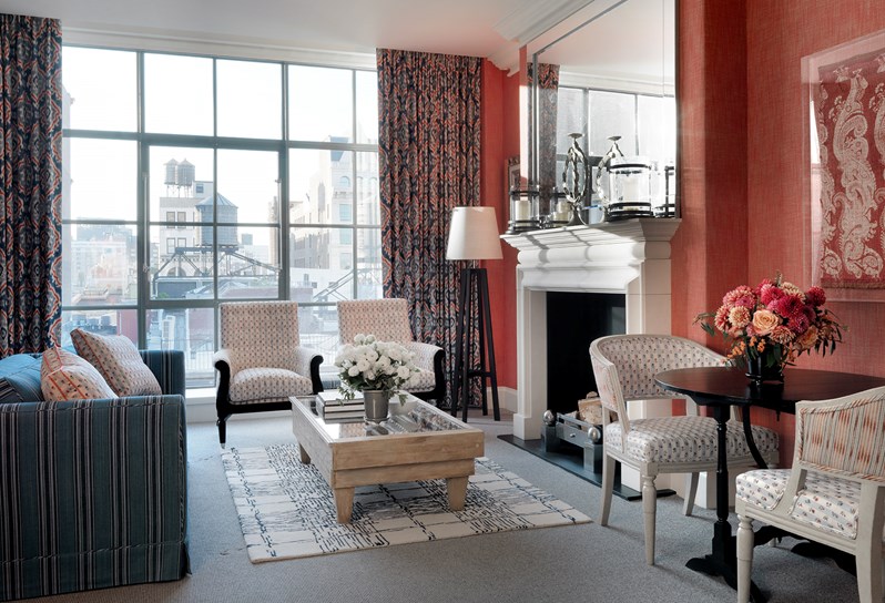 The living room with fresh flowers, several chairs and a sofa in a one bedroom suite at the Crosby Street Hotel with a colourful interior design and floor length windows with views of the SoHo neighbourhood.