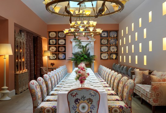 The Orangery set up for private dining for 25 people on one long table with beautiful flower arrangements, with comfortable, padded chairs in patterned fabric around.