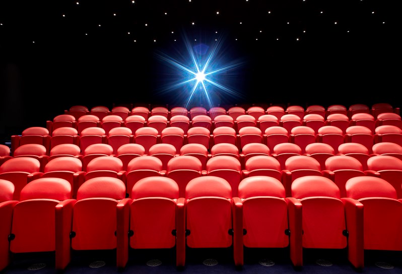 The large screening room at Soho Hotel. Rows of red leather cinema seats. In the background is the light from a projector.