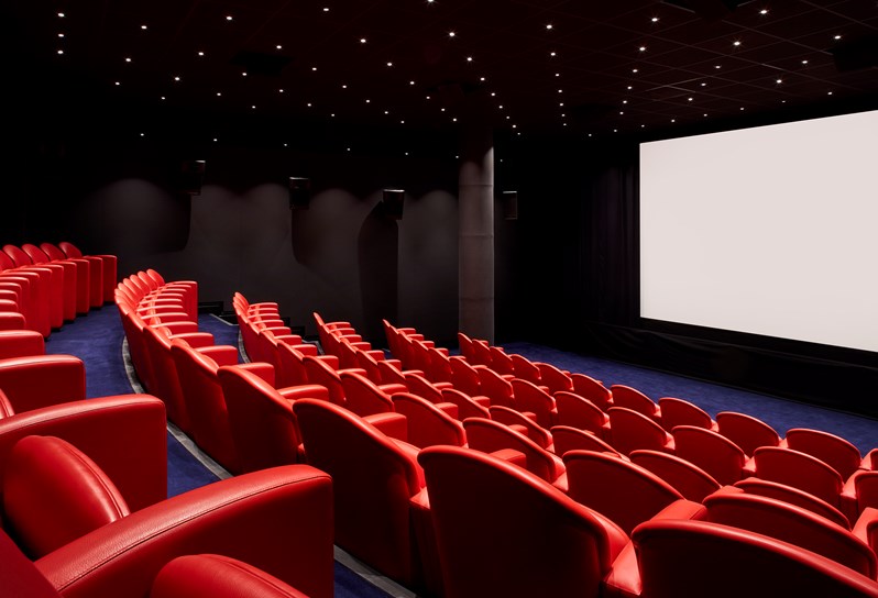 Large screening room at Soho Hotel. Tiered rows of red leather seats face towards a blank cinema screen.