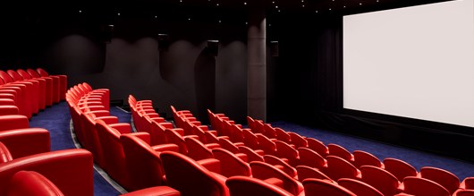 Large screening room at Soho Hotel. Tiered rows of red leather seats face towards a blank cinema screen.