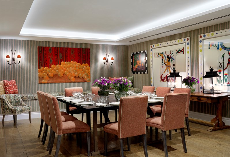 The beautiful Vanessa Bell Room setup for a dinner on a long tables with orange chairs. There is beautiful bright artwork on the walls and flowers decorating the table.