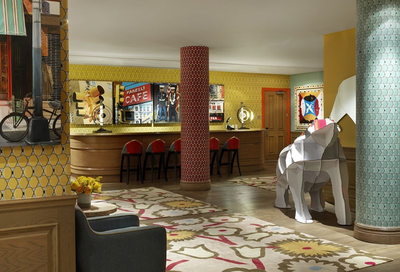 The Events floor lobby with colourful wallpapers and art looking towards a bar with a row of bar stools against a long oak bar.