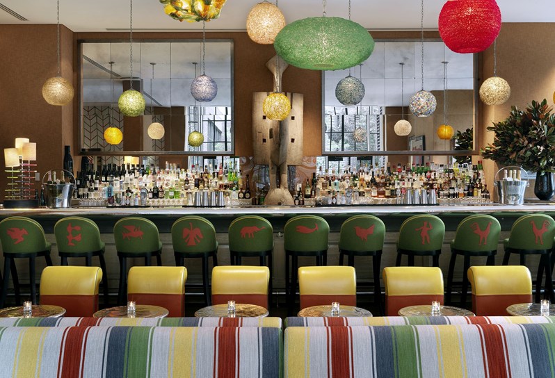 A long colourful bar serving with bold striped lunge seating and serving breakfast, lunch, dinner, afternoon tea and cocktails all day long.