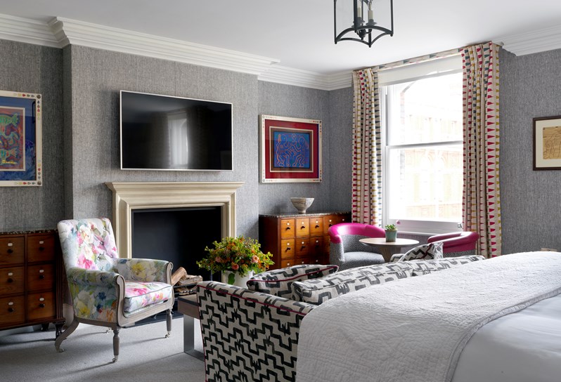 The living area at the bottom of a bedroom. There is a black and white sofa facing a multi coloured armchair and fireplace with a large television above.