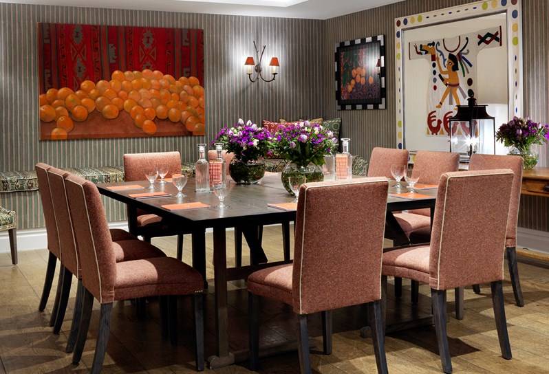 The beautiful Vanessa Bell Room setup for a meeting with orange chairs. There is beautiful bright artwork on the walls and flowers decorating the table.