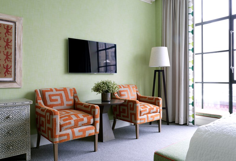 A beautiful bedroom with floor to ceiling windows, chairs with a graphic orange colour and walls in green linen.